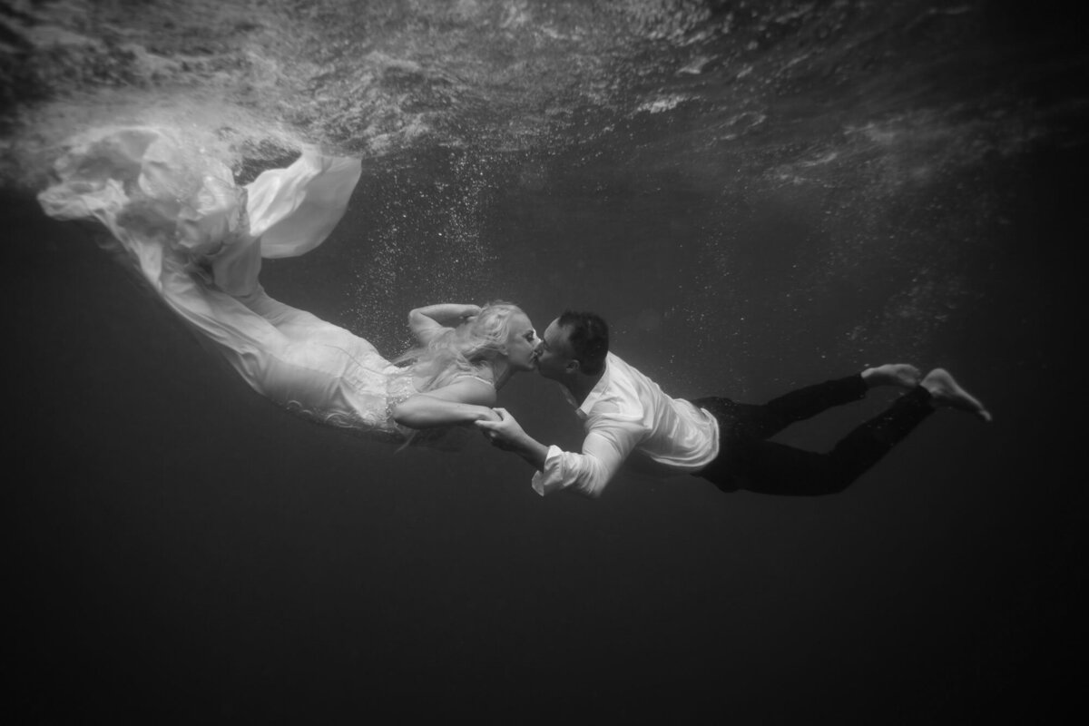 bride and groom kissing underwater in black and white