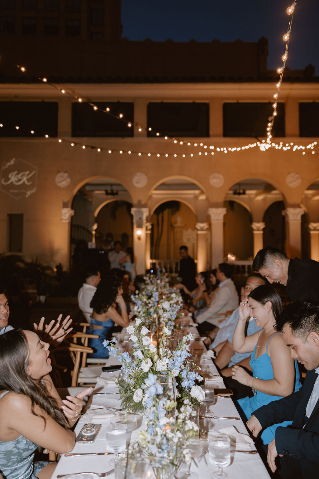 Photo down the center of a long rectanlge table with guetss mingling during reception on each side and laughing