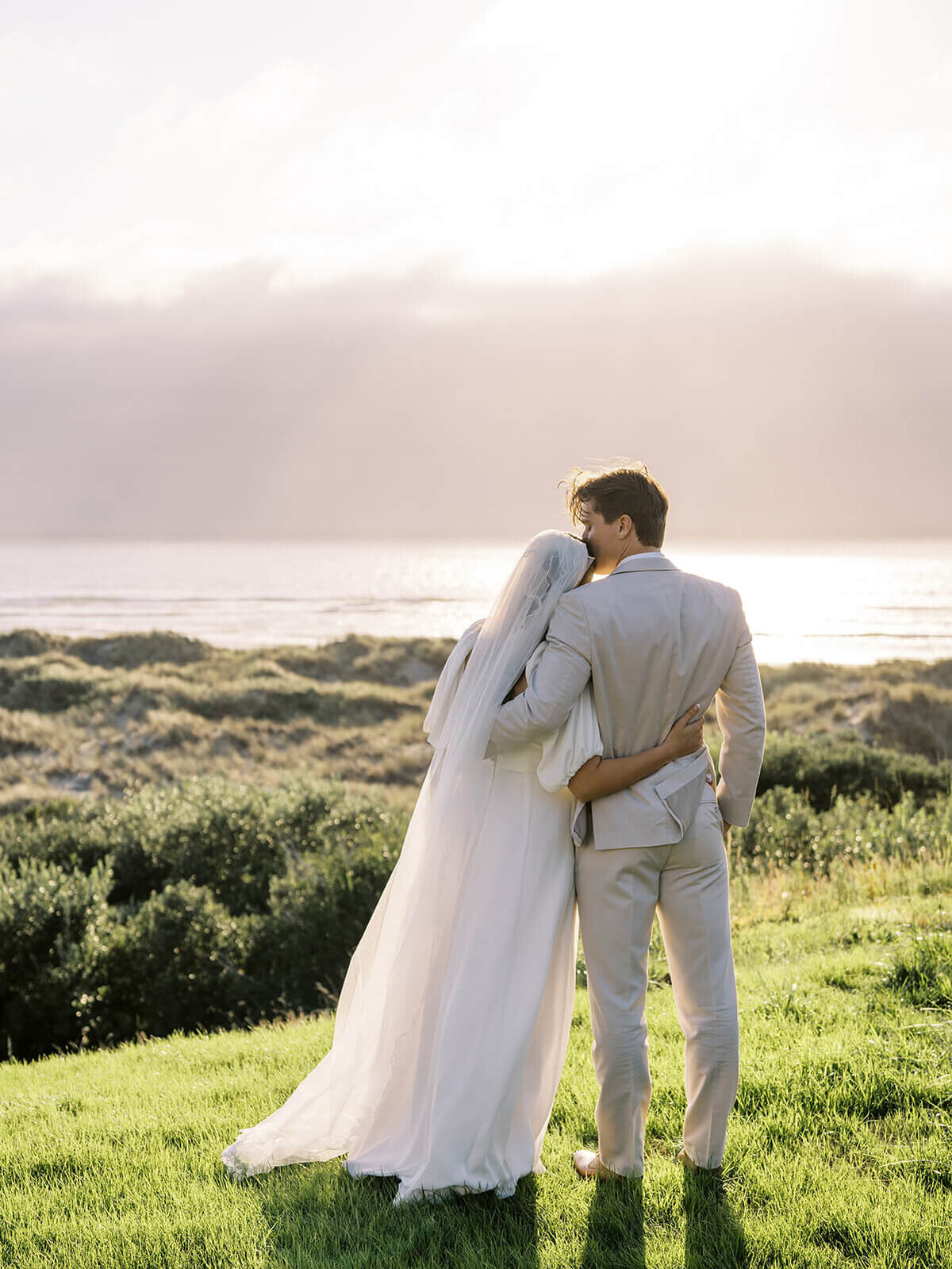 A bride leaning against a groom with him kissing her forehead. 