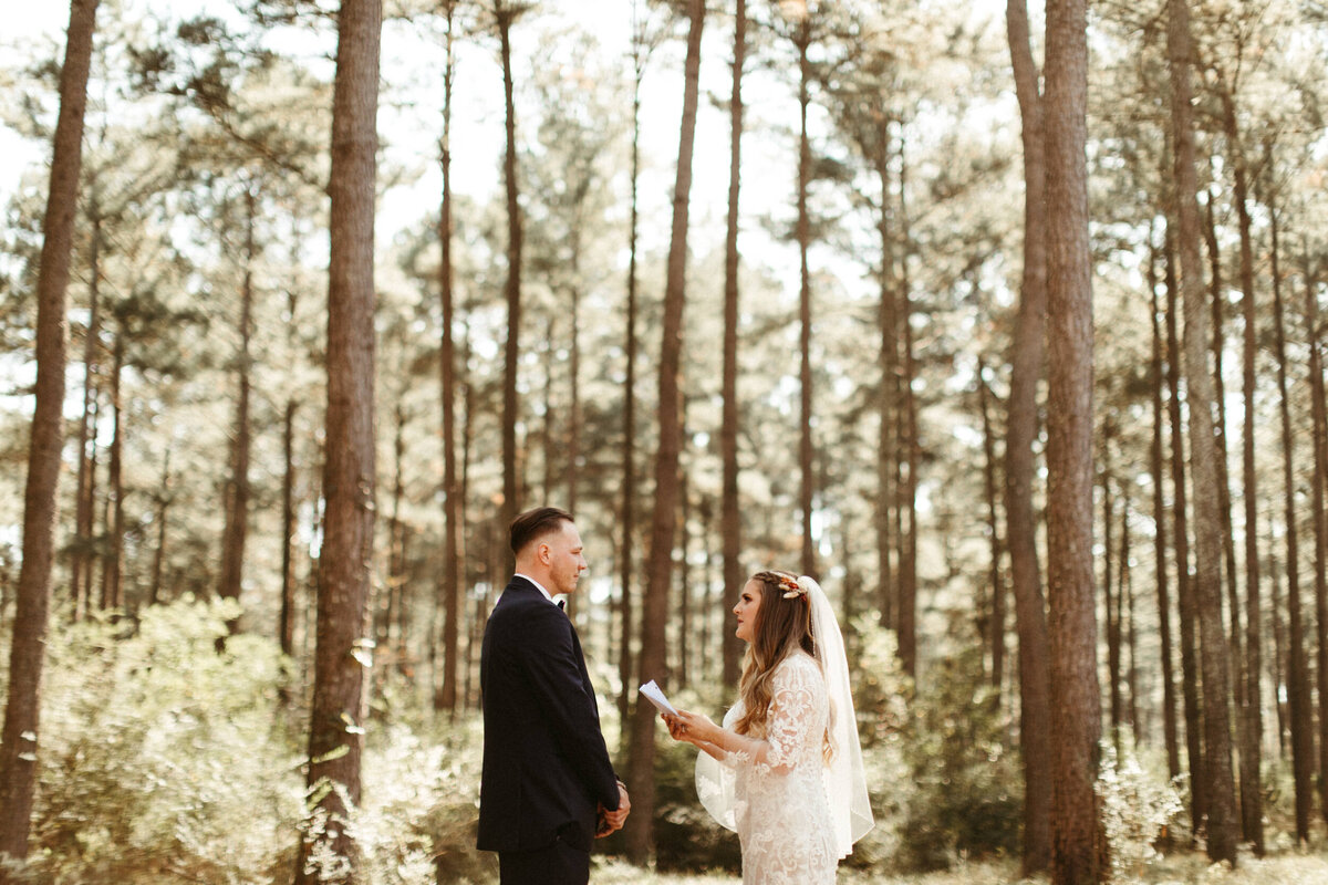 Bride and groom standing in the forest surrounded by tall trees and exchanging their personal vows