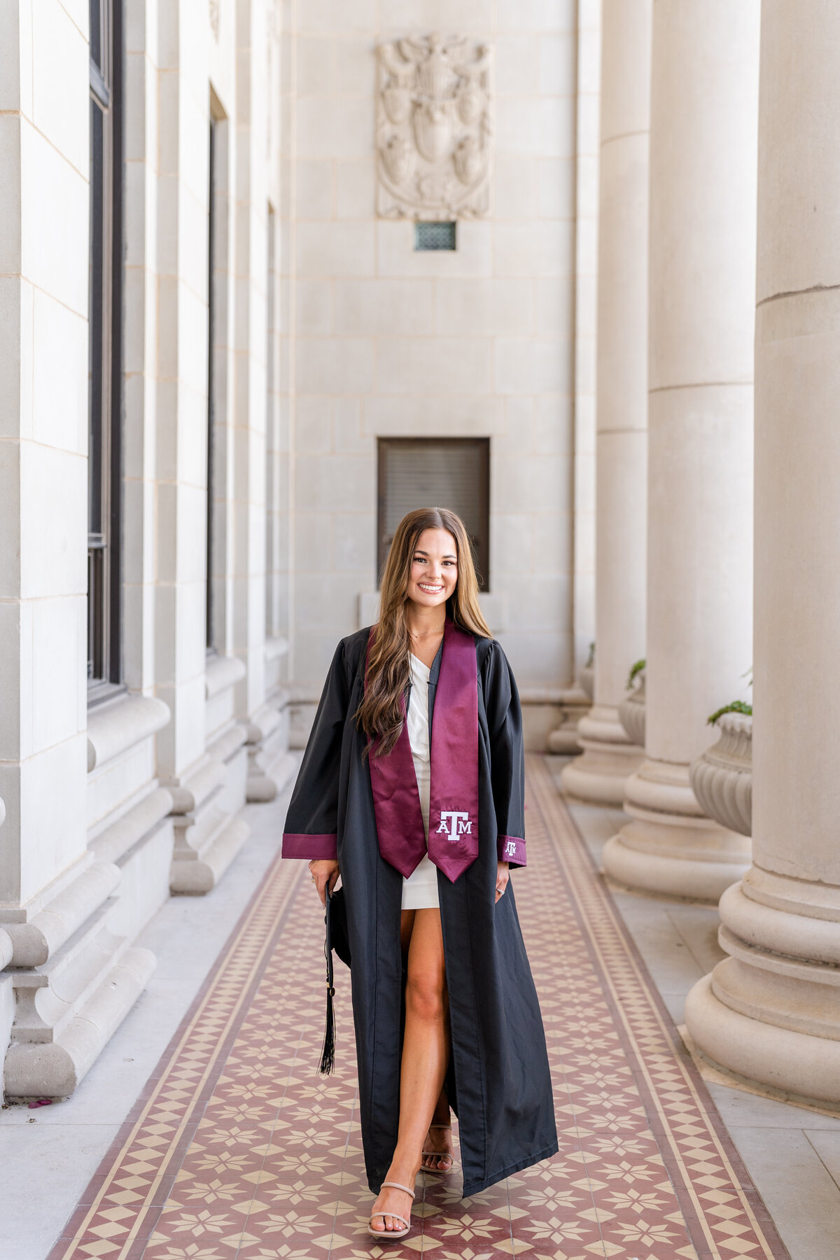 Texas A&M senior girl walking and holding grad cap while wearing gown and Aggie stole in the columns of the Administration Building