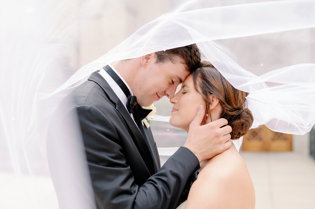 bride and groom touching foreheads while wrapped in the bride's veil