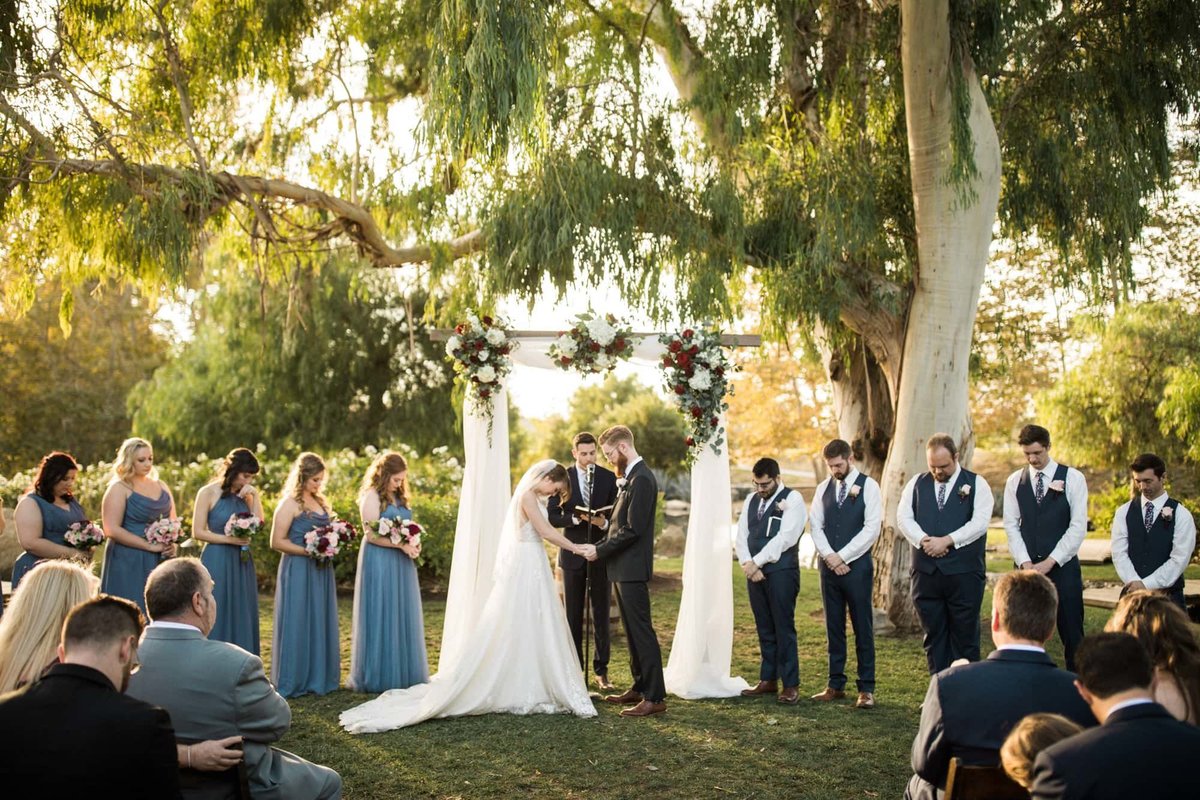 Officiant offers a prayer as bridal party and wedding guests bow their heads