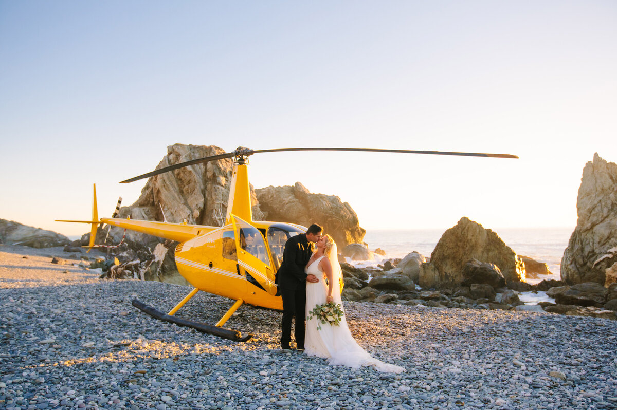 A bride and groom kiss in front of a helicopter on Catalina Island