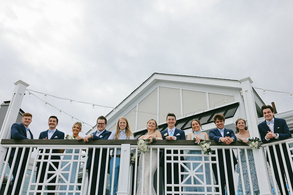 Joyful wedding party gathers together through on a balcony overlooking the Atlantic ocean in Nahant, MA.