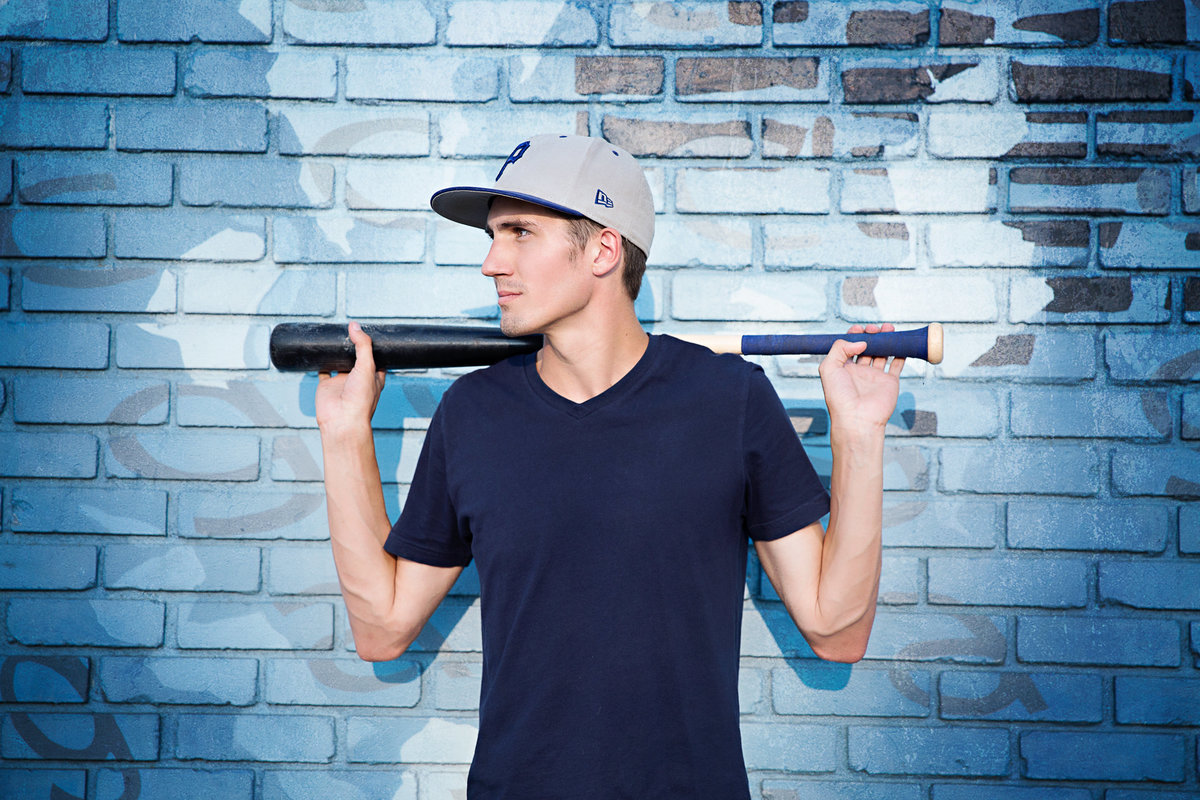 High school boy poses with a baseball bat and hat in an urban setting