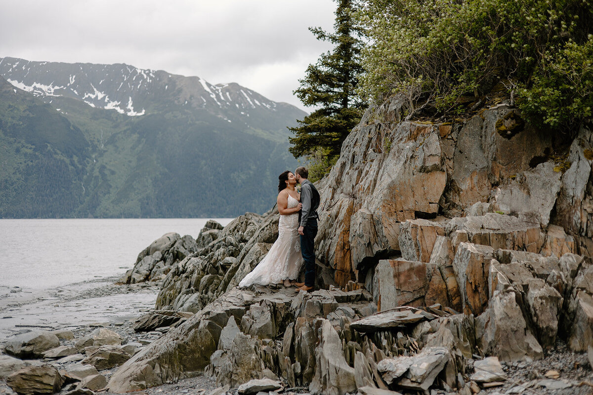 Elopement couple embraces on Alaska rock shoreline.