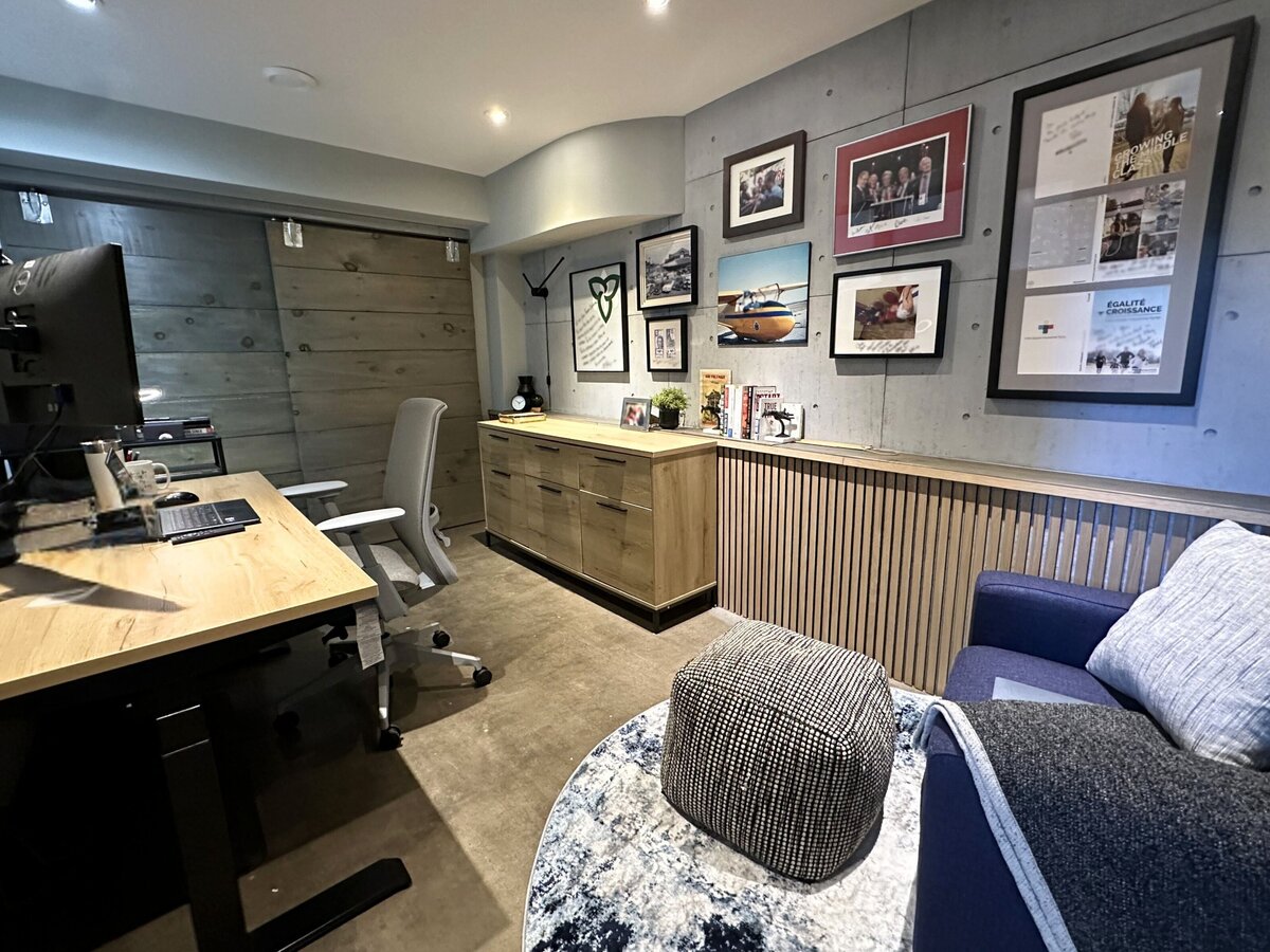 Urban industrial-style home office with concrete walls, wood cabinets, standing desk, and gallery wall art, softened with squishy armchair, pouffe and round area rug designed and installed by Urbanomic Interiors, Westboro (Ottawa.)