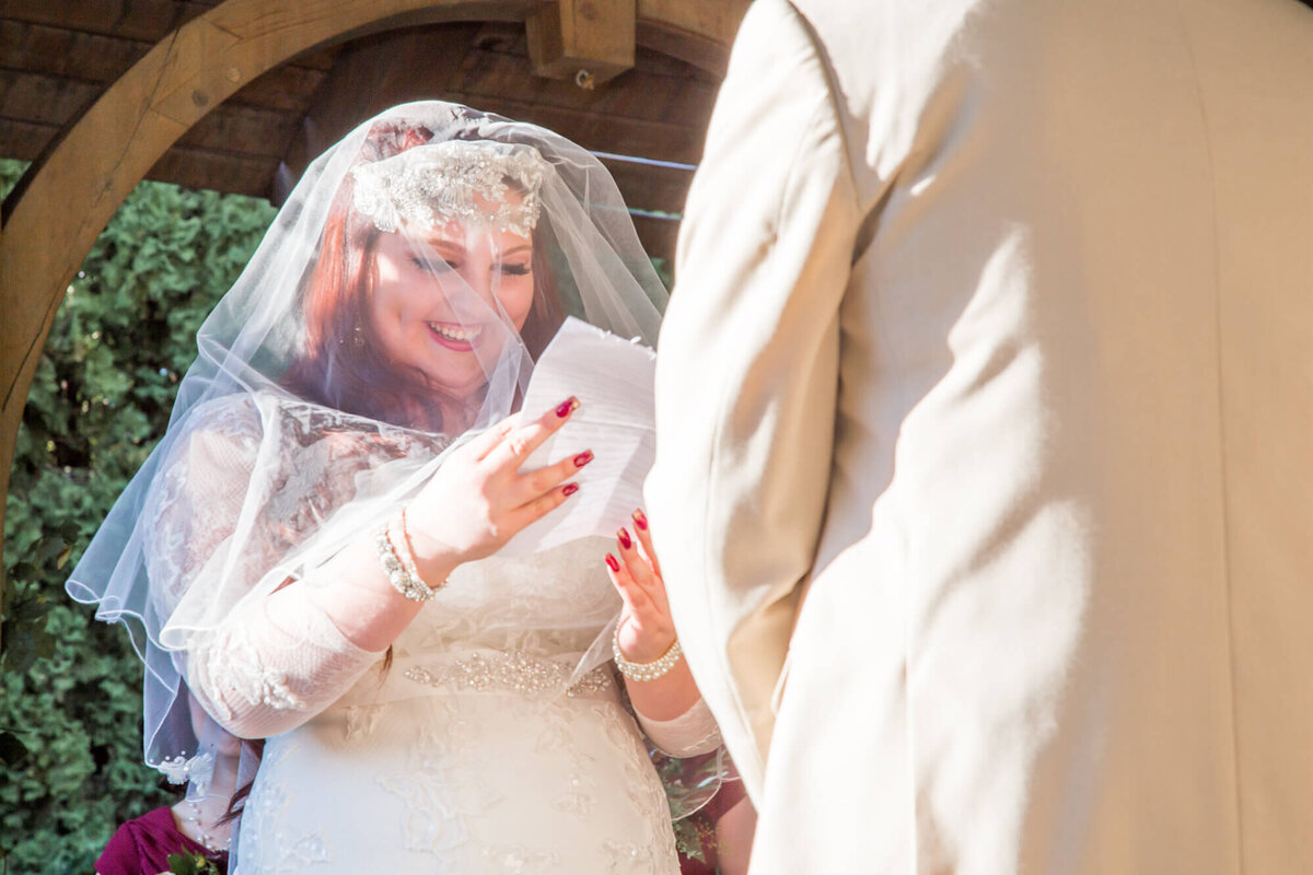 happy redheaded bride reading her vows during her beautiful garden wedding ceremony