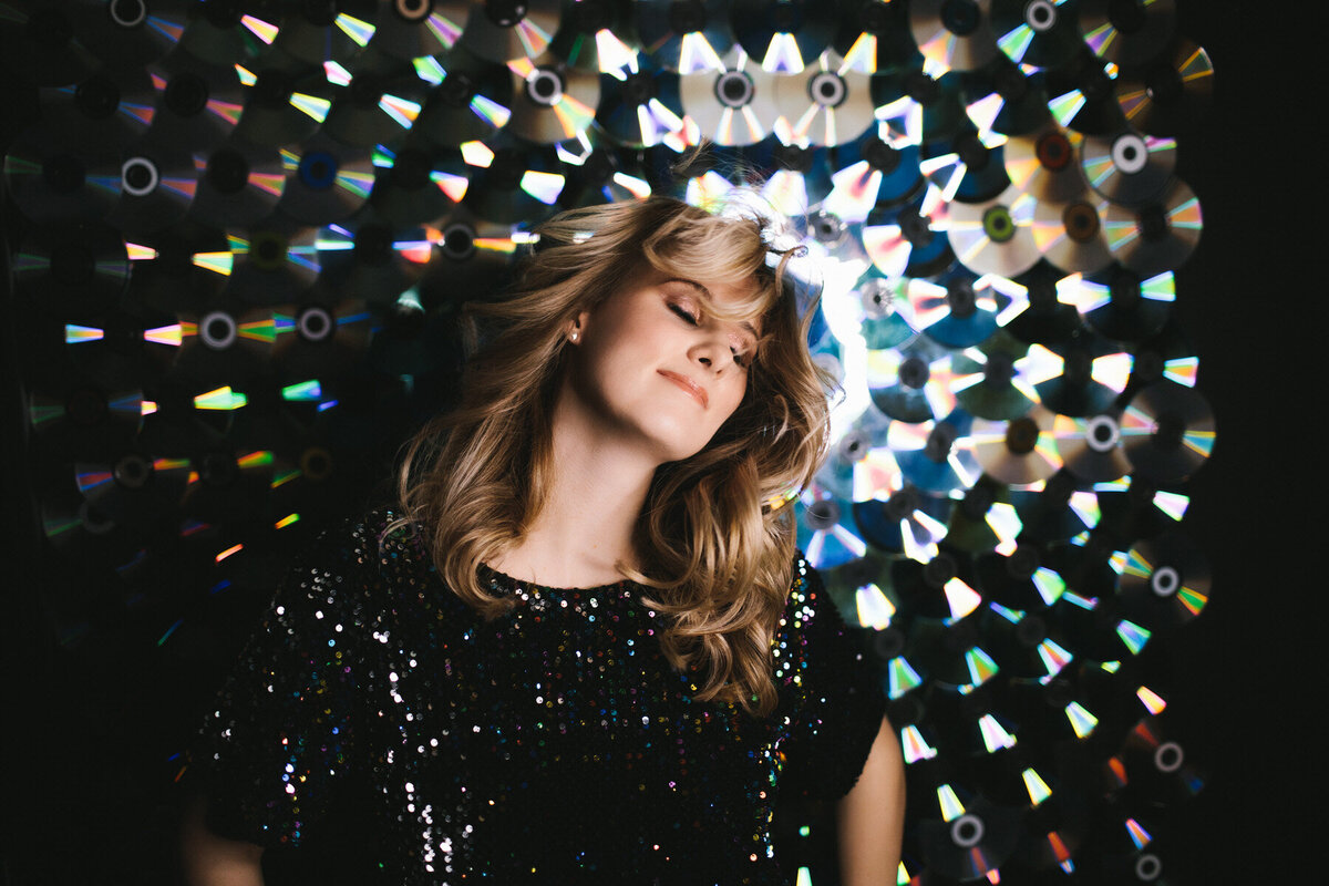 portrait of woman wearing sparkling black shirt posing in front of CD wall