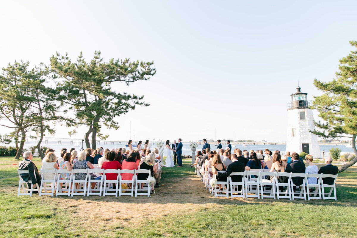 Wedding ceremony with bride and groom standing seaside in front of a lighthouse in Newport Rhode Island