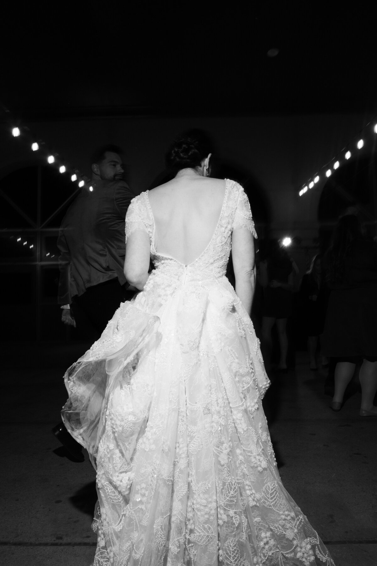 Black and white image of bride walking into reception under string lights