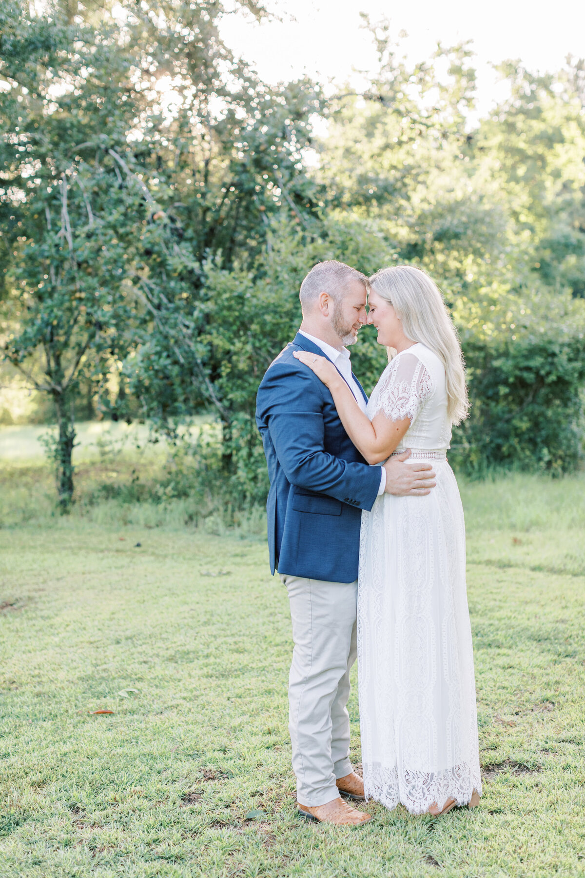 A couple puts their foreheads together while standing in front of  the tree.