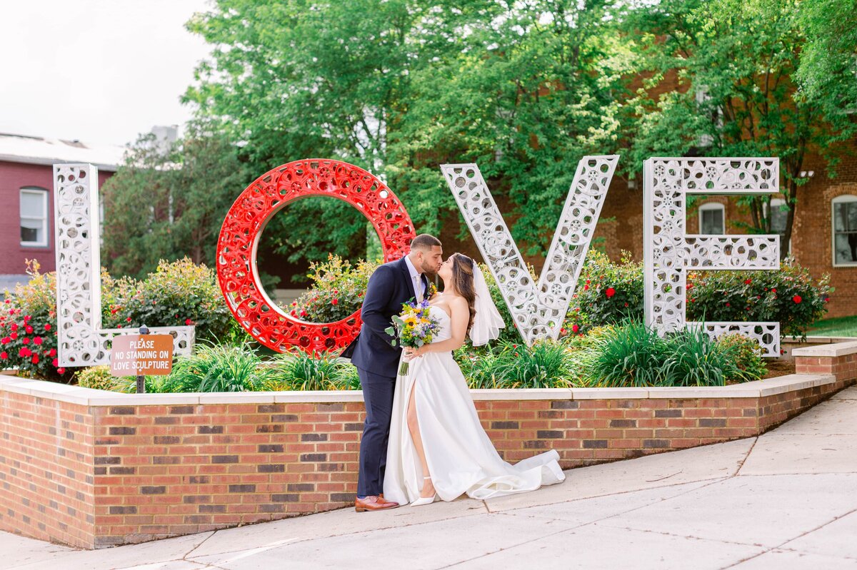 Bride and Groom kissing in front of Love Sign for wedding in Culpeper, Virginia. Captured by Bethany Aubre Photography.