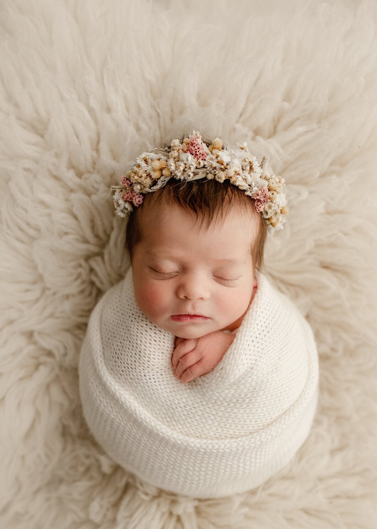 beautiful new baby girl in a cream wrap in photography studio