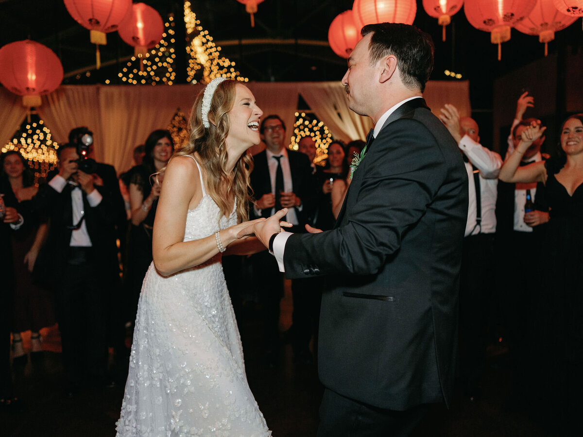 The newlyweds share a joyful dance on the wedding dance floor, surrounded by glowing red lanterns and celebrating guests.
