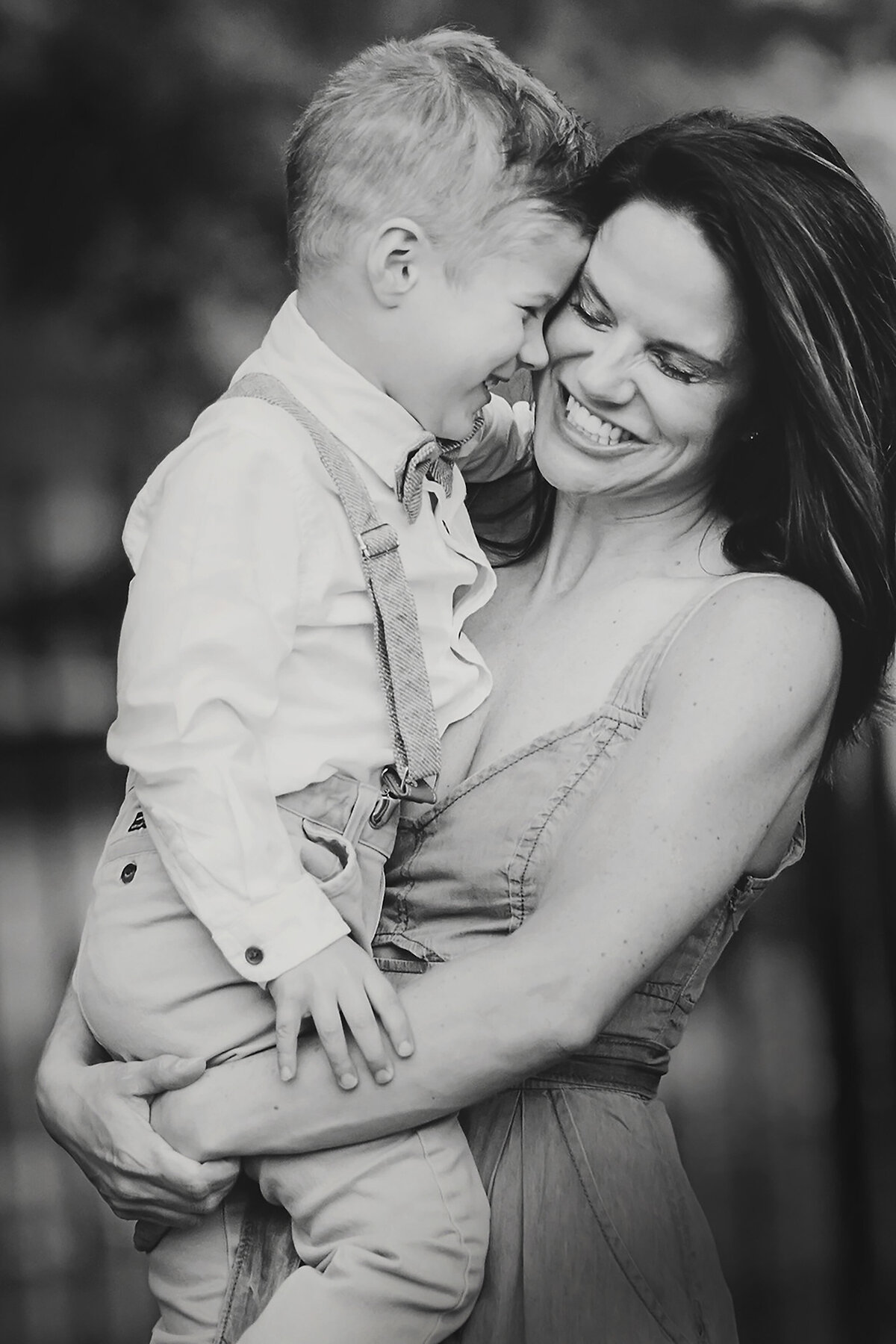 Black and white photo of mother and son. She is holding him and he is leaned into her, both smiling.