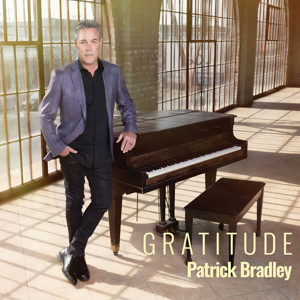 Jazz pianist album cover Gratitude by Patrick Bradley standing beside piano large windows behind