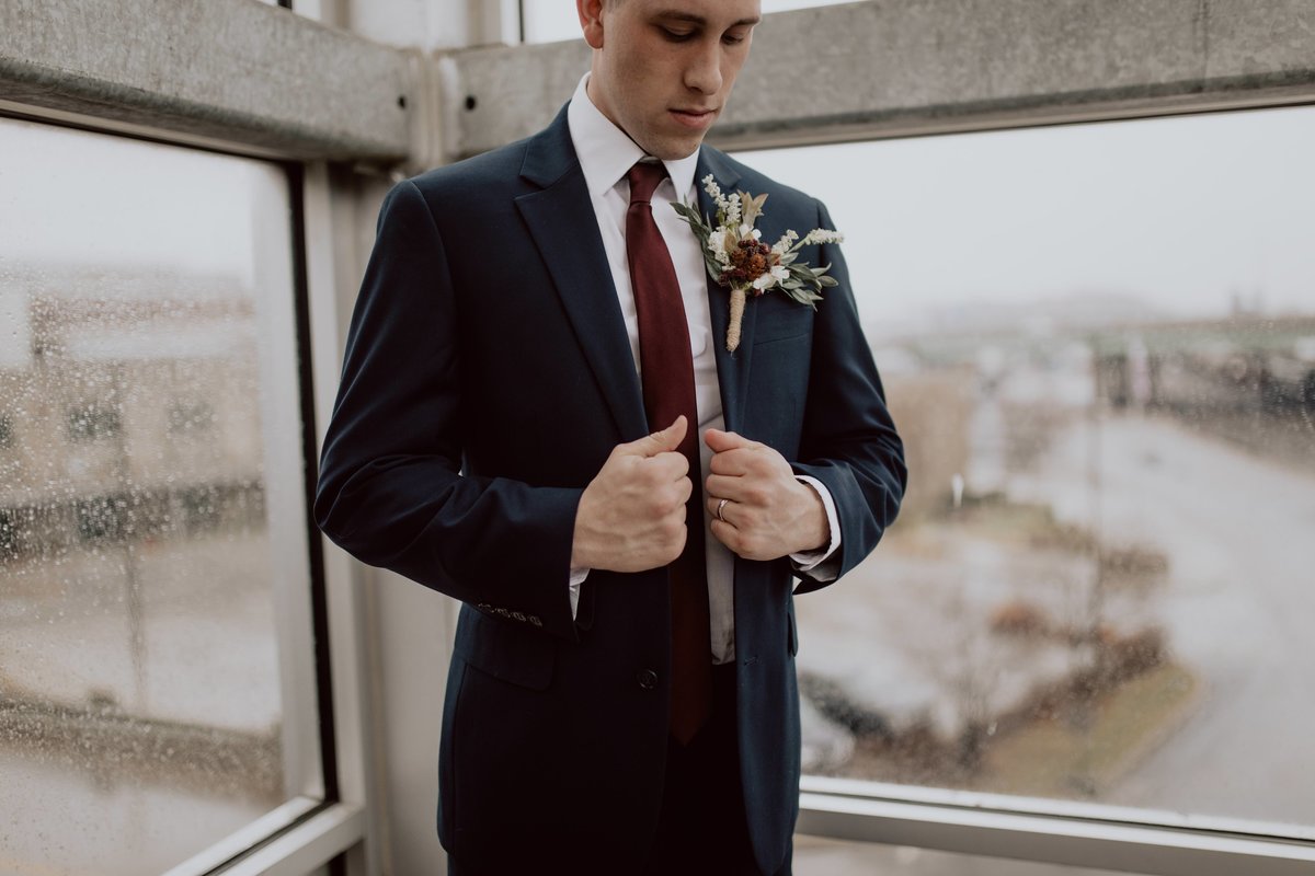 Groom getting ready, buttoning up jacket for wedding  on a rainy day in Kansas City.