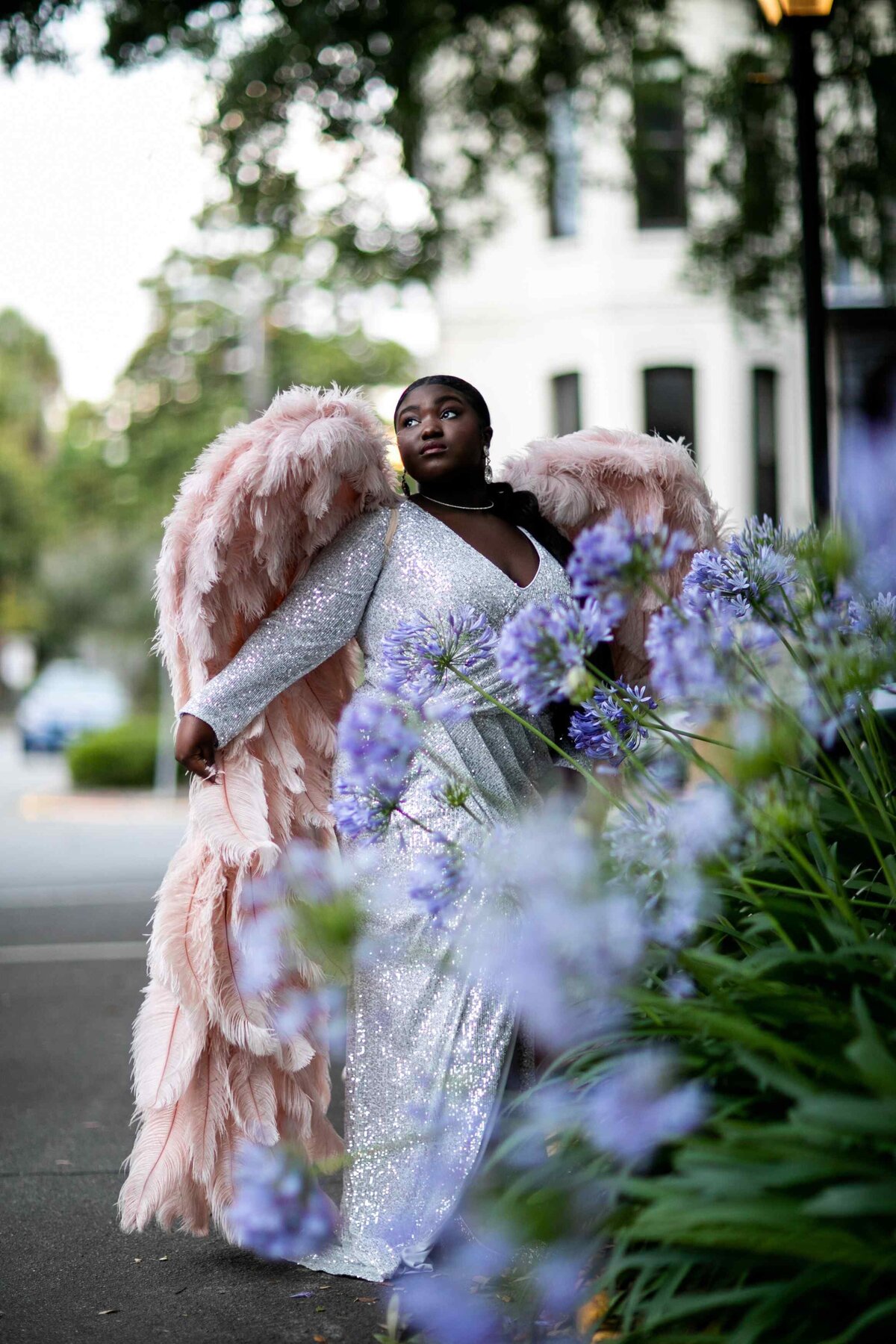 senior posed behind bush and flowers wearing gown and wings