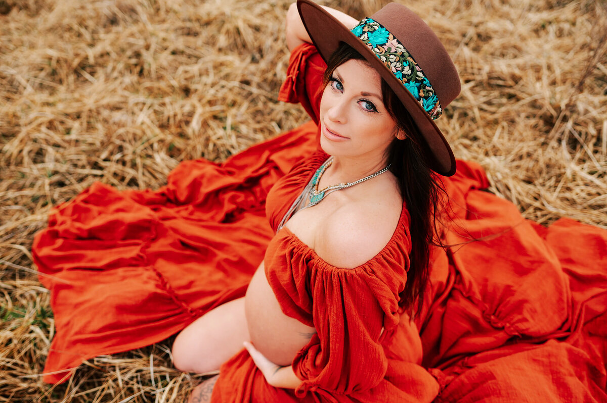 pregnant mom kneeling in field in red dress enjoying maternity photography in Branson