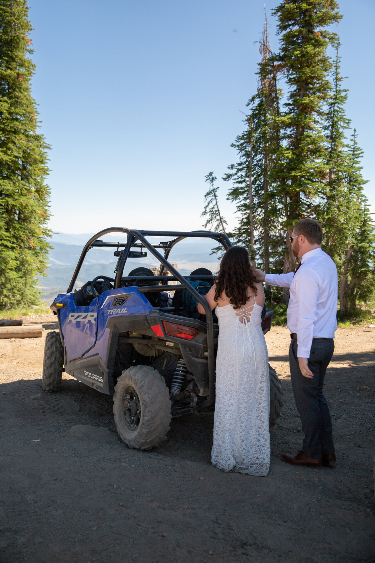 A bride and groom stand behind a side-by-side on their elopement day.