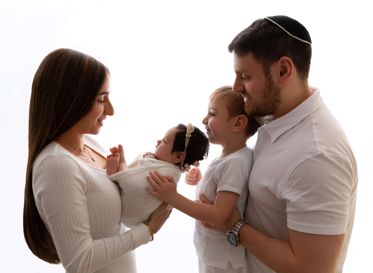 Parents and older sibling admiring their newborn baby, captured in a heartwarming family newborn session in Queens