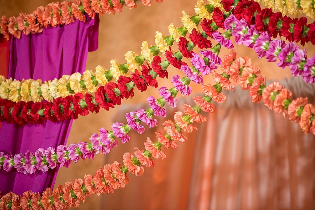 Coral, pink, red and yellow carnation garlands deocrating a magenta and peach mandap in Nashville, TN at an Indian Wedding