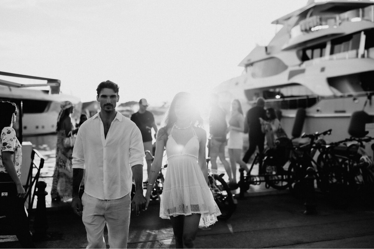 Bride and Groom holding hands walking past the boat docs with large yachts behind them.