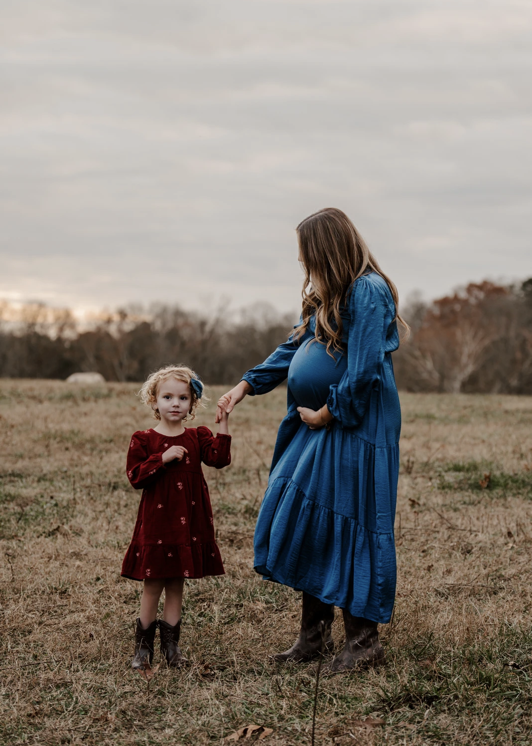 Maternity portrait—mother standing in a field with her children embracing her belly in a quiet, emotional moment.