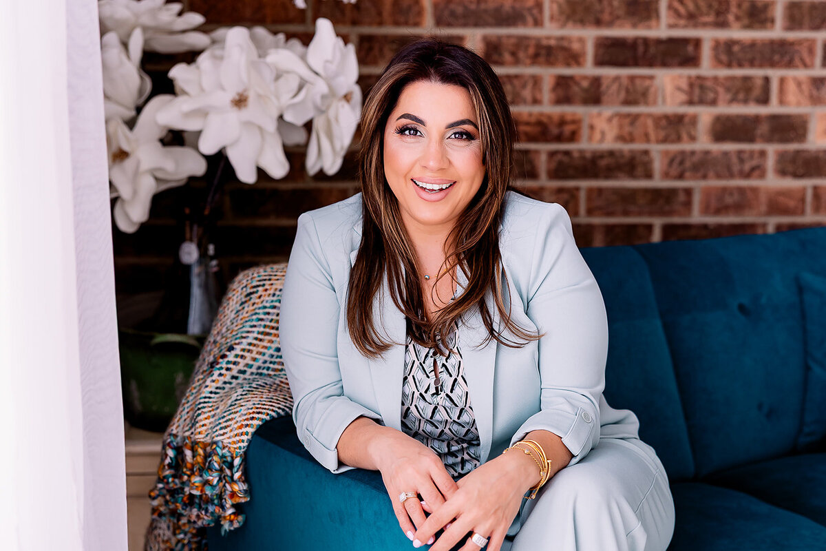 Woman sitting and leaning over arm chair while wearing a light blue pant suit