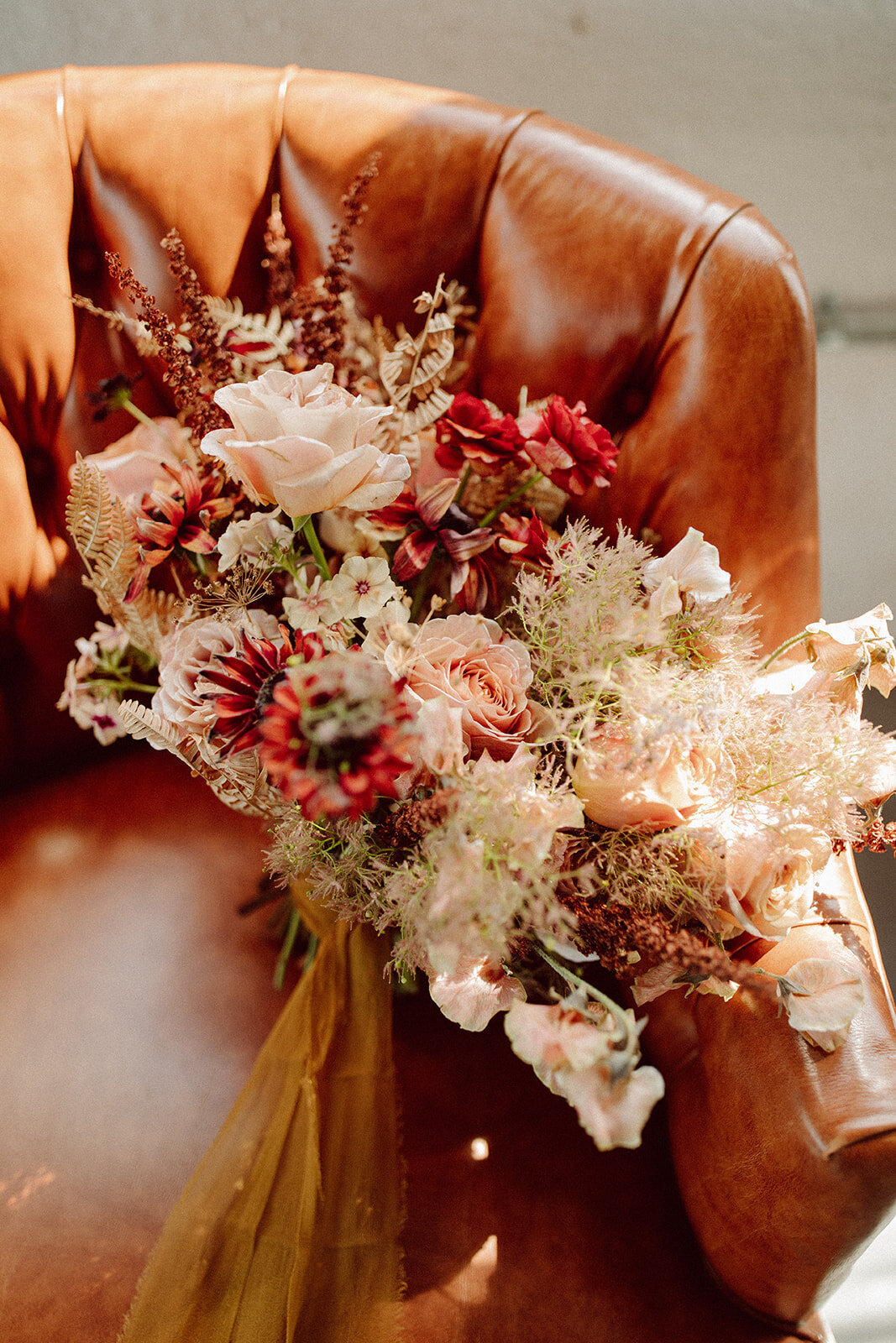 Arrangement of cream, blush and wine-colored flowers atop a leather chair.