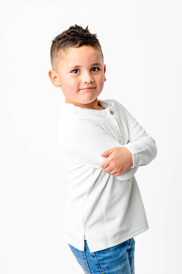 Boy poses with folded arms in a bright white photos studio.