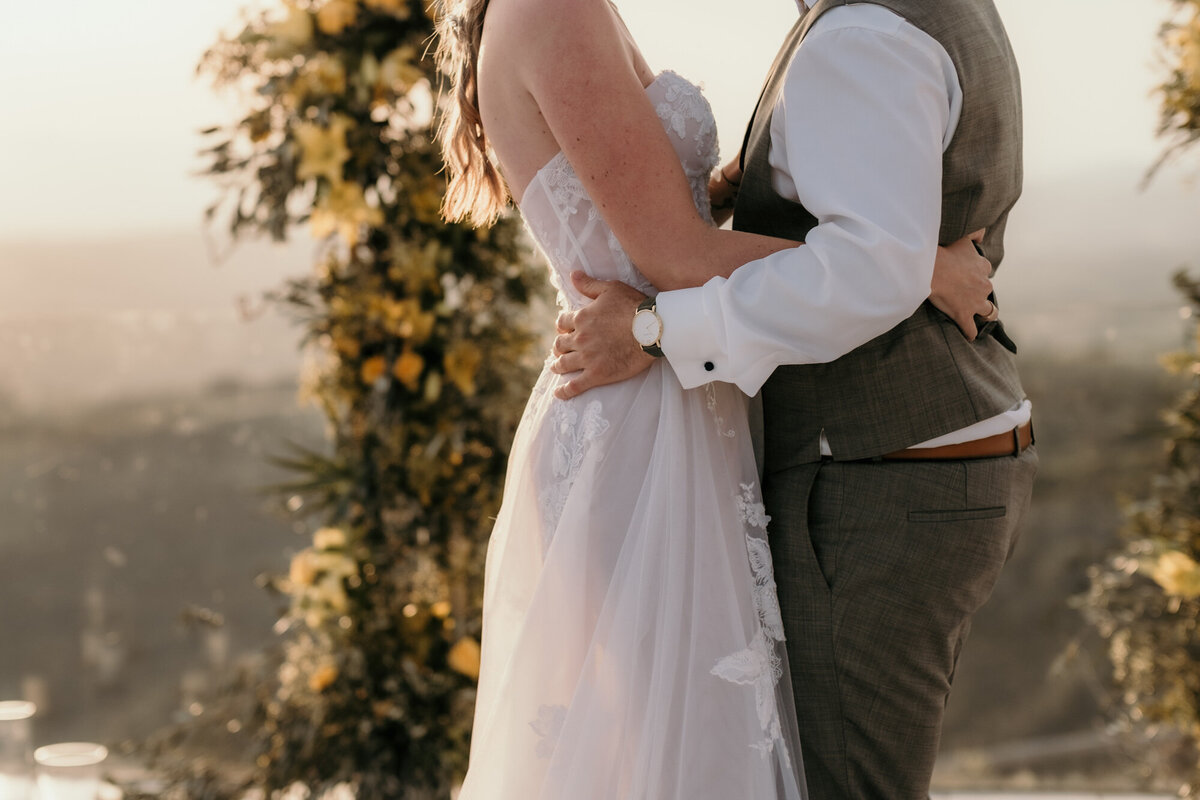 Vor den gelben Rosenstöcken stehend hält sich das Hochzeitspaar eng im Arm.