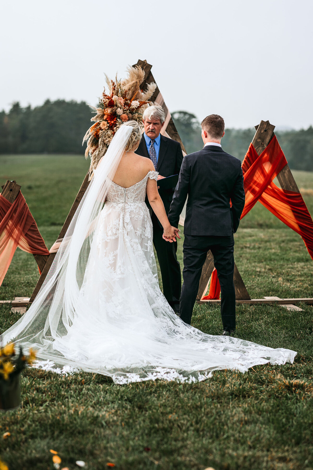 Bride and groom facing officiant as he speaks to them in open field at Sanborn Hill Farm in NH by Lisa Smith Photography