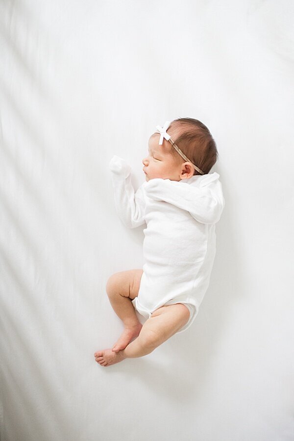 baby sleeping in crib with white onesie on and bow DC Newborn Photographer Emily