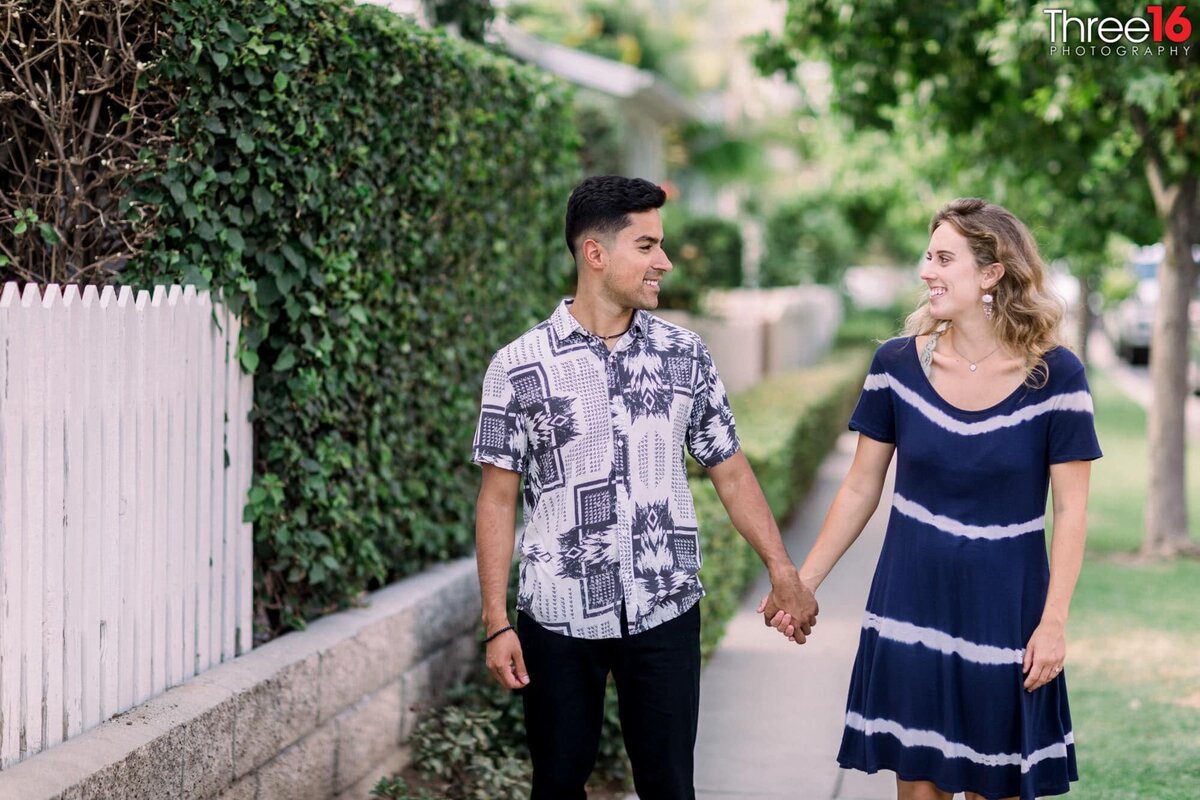 Engaged couple talk as they walk along a Downtown Brea sidewalk holding hands