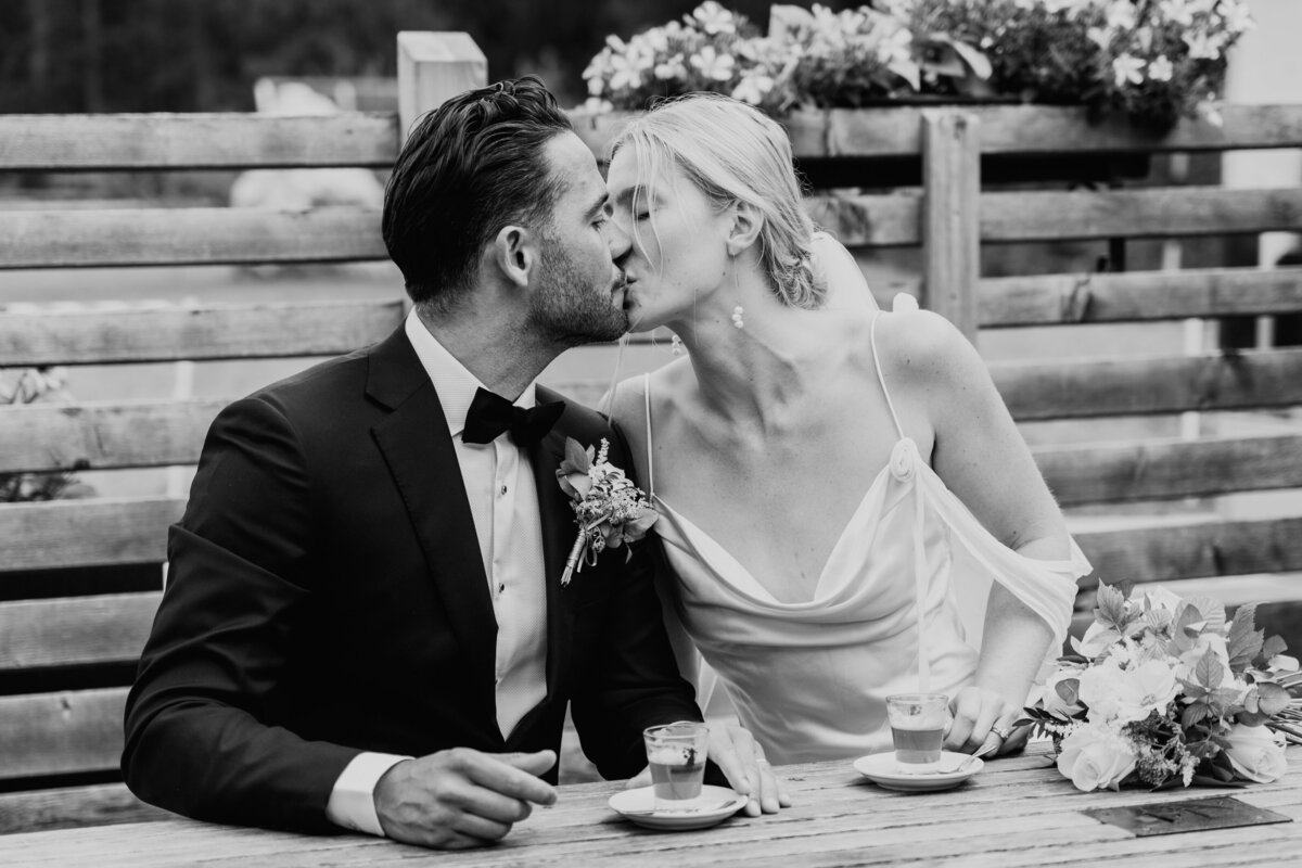 Bride and groom kissing at reception table in black and white