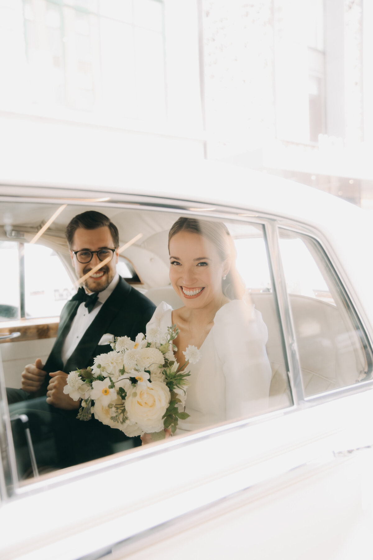 A bride and groom smile in a limousine on their way to their Atwater Club wedding.