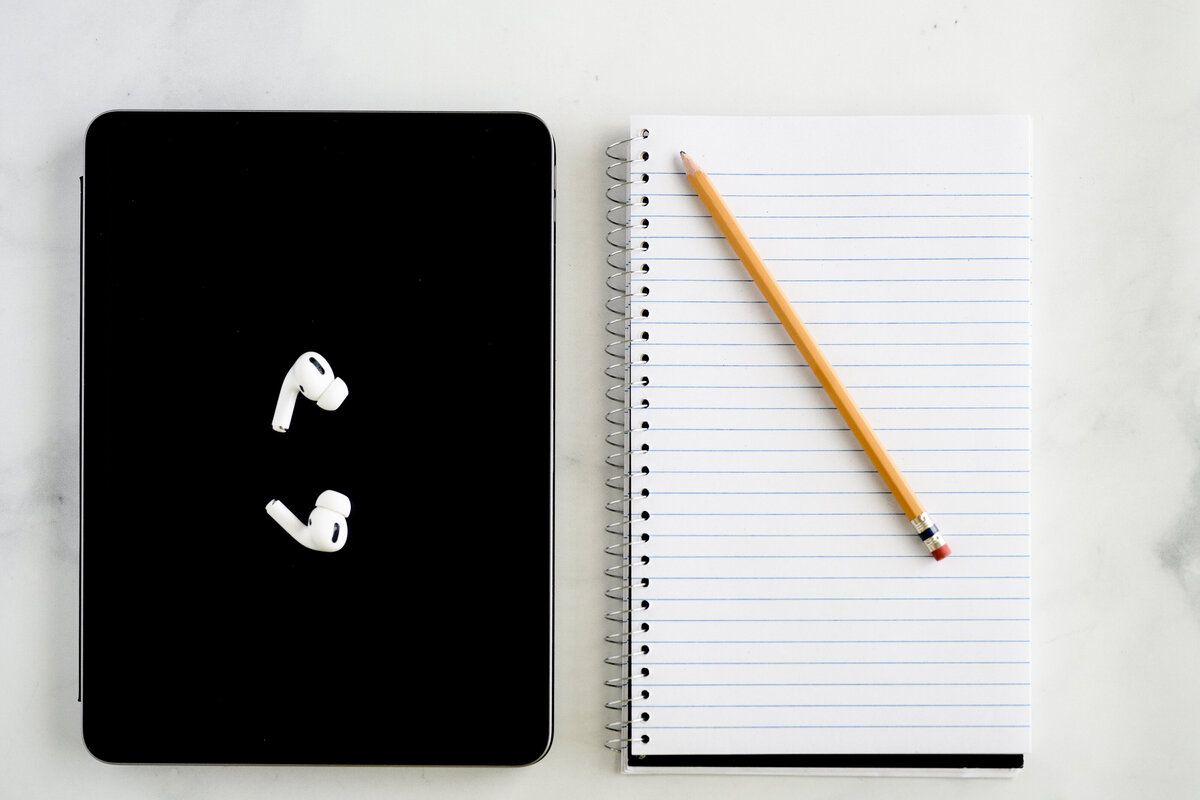A denver product photographer and brand photographer in Denver takes a photo of a flatlay of an ipad and airpods and journal with pencil for branding photos and branding pictures.