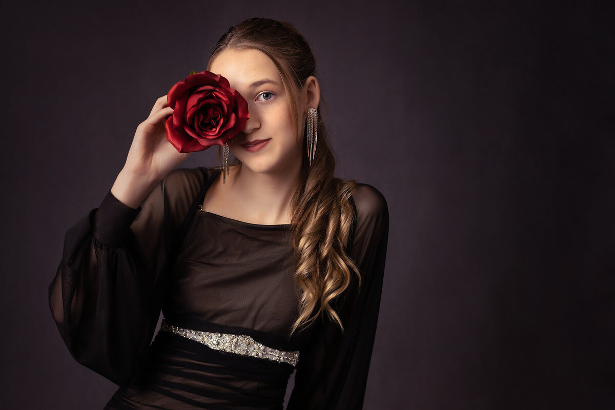 A senior holds a vibrant red rose to her face in a fashion-forward, elegant portrait. Captured by a Dallas senior photographer.