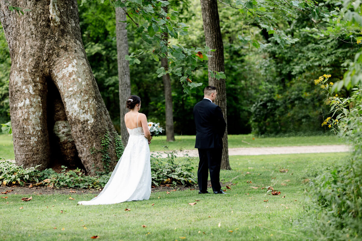 Bride and groom standing back-to-back during a first look in a wooded setting