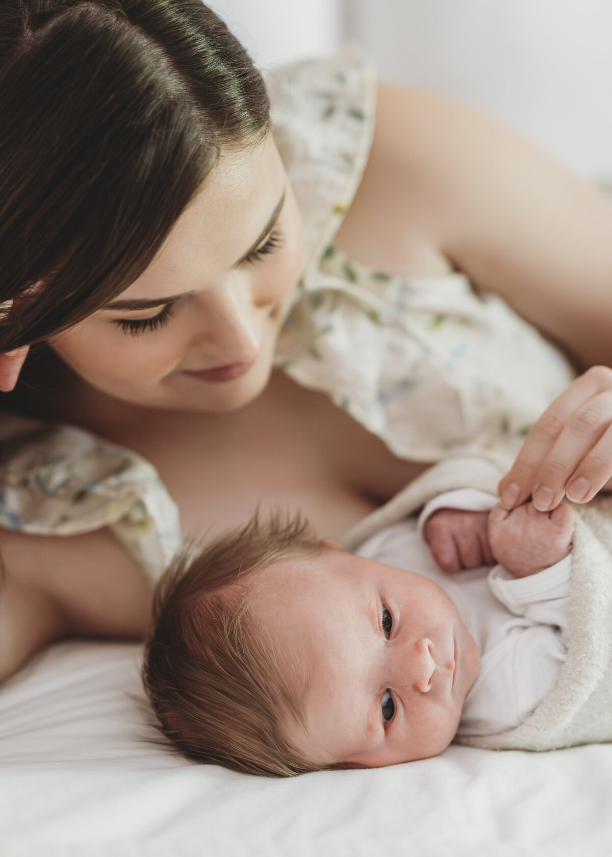 Mother lying on a bed gently holding her newborn’s hand during a lifestyle newborn session in Kansas City.