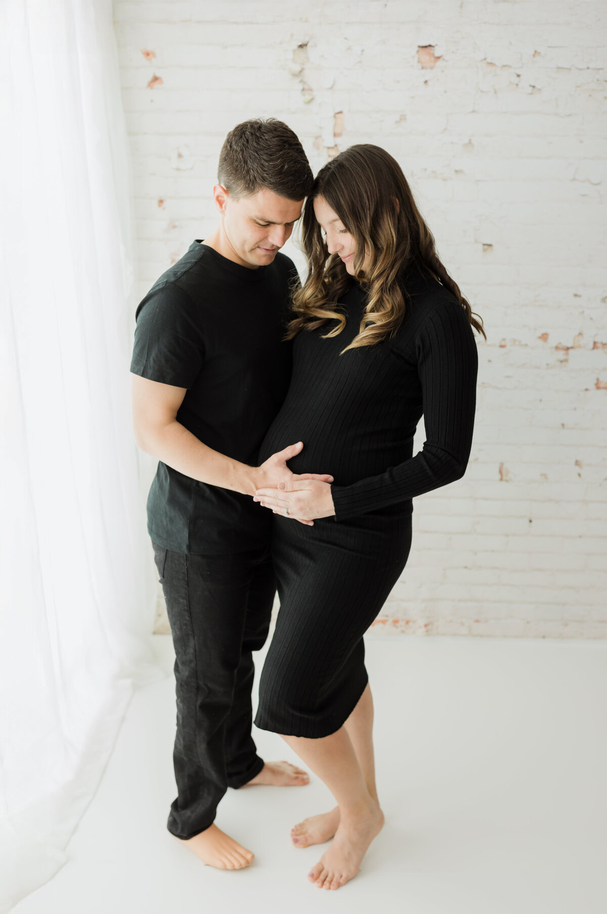 husband and pregnant  wife in black maternity dress holding baby bump for maternity photoshoot
