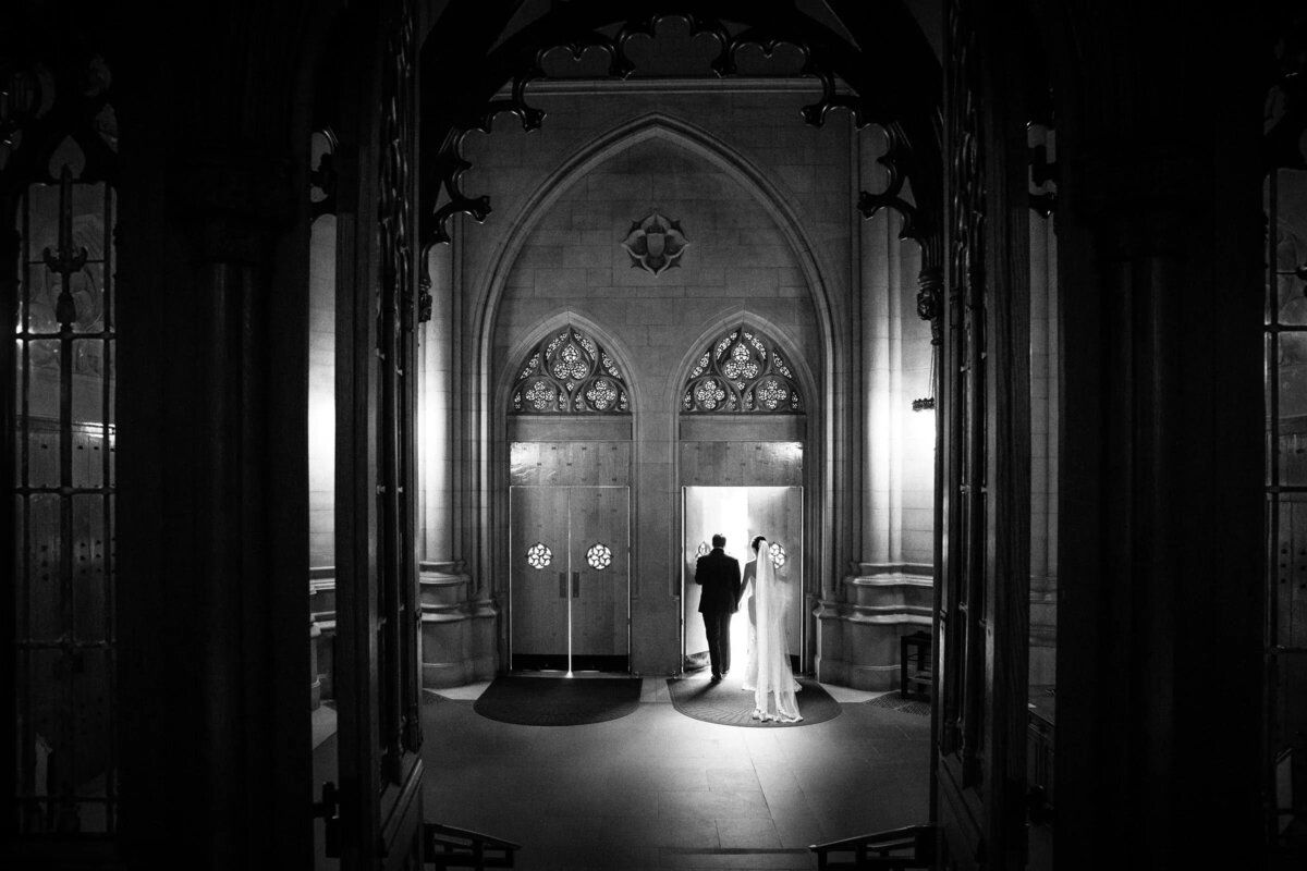 Bride and groom standing in a grand doorway, sharing an intimate moment, enveloped in the soft light of the interior