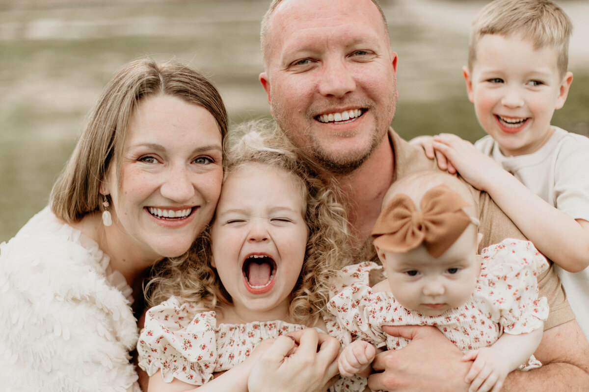 Family of 5 laughing and smiling at the camera. 