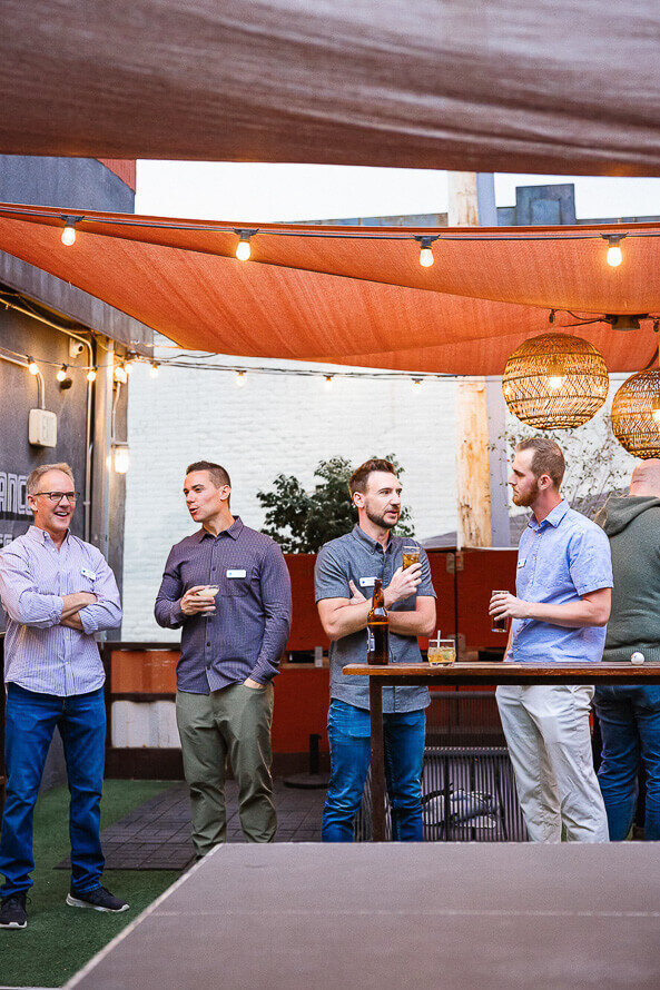 Group of four men holding drinks and chatting.