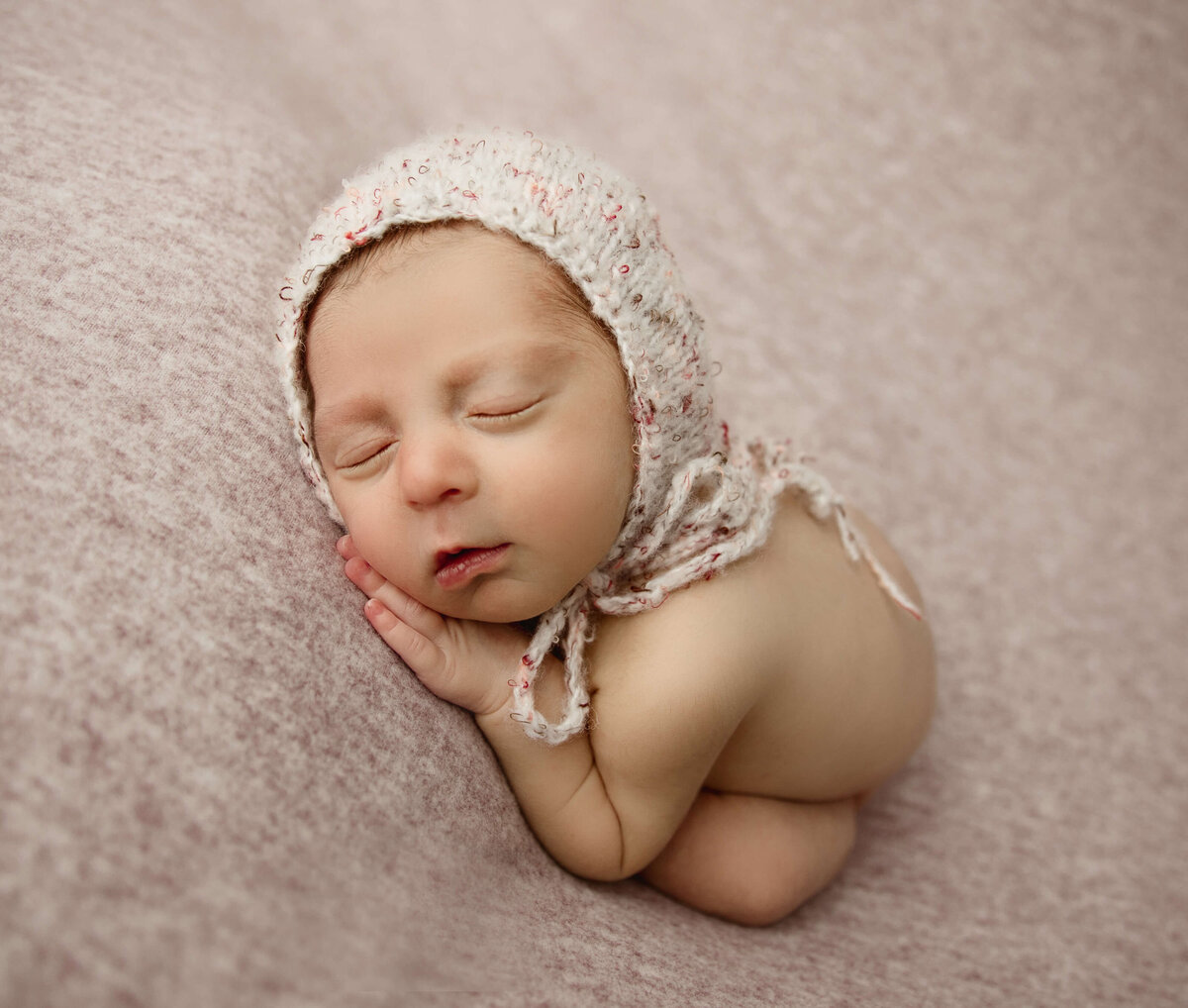 Photo of a newborn baby girl with a knit bonnet in an Erie PA photography studio