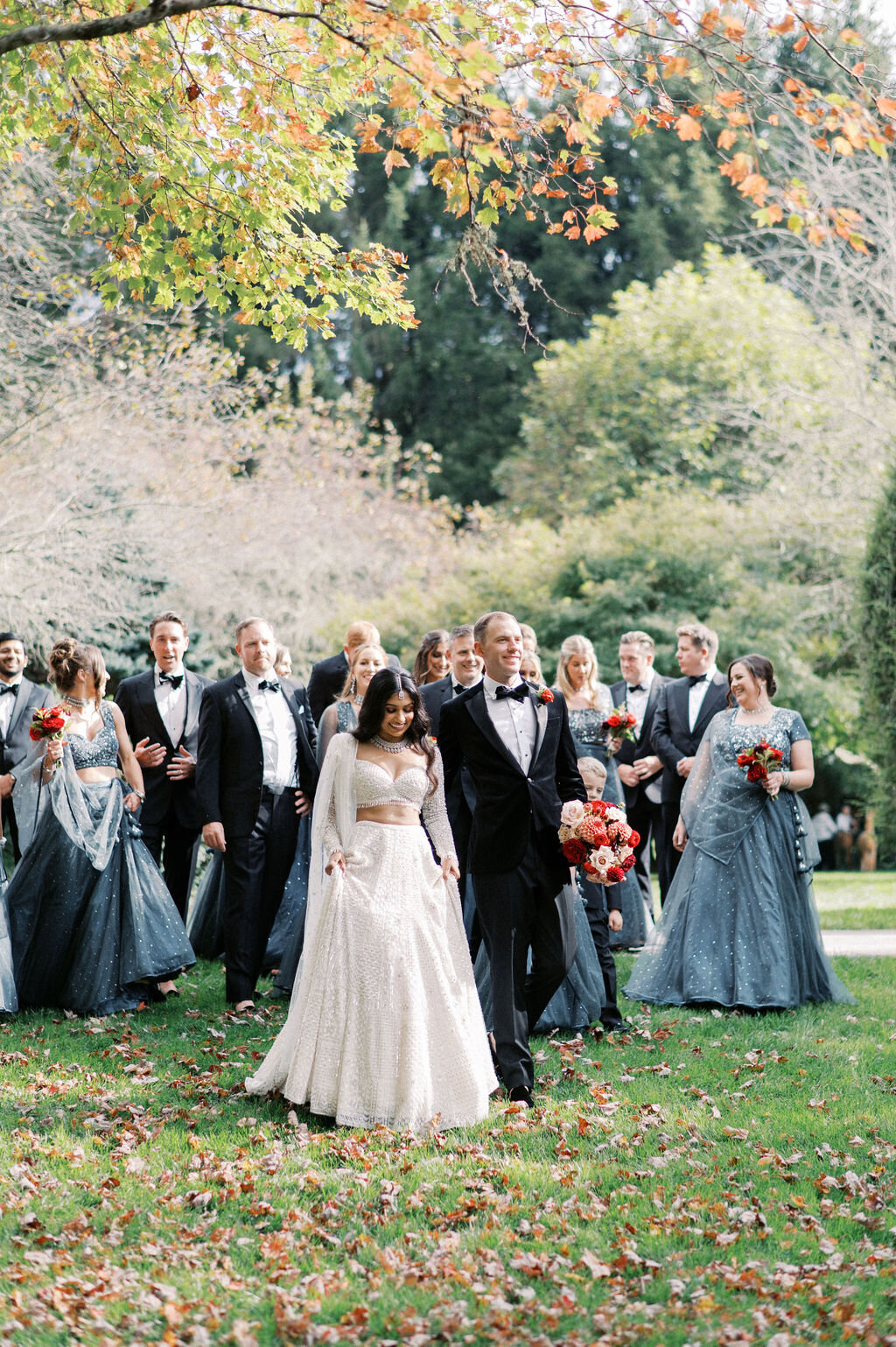 Full wedding party portrait outdoors with bridesmaids in slate blue gowns and groomsmen in tuxedos at a fall wedding in Highlands, NC.