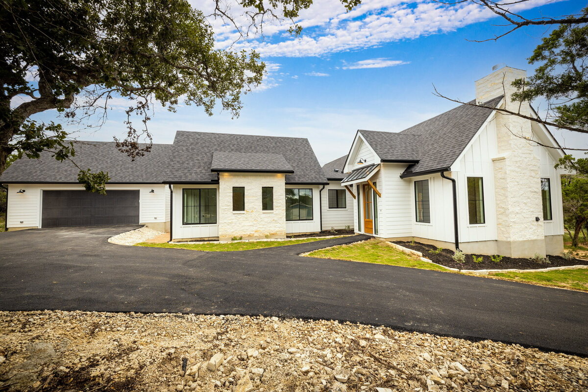 driveway to white board and batten and limestone house in the texas hill country